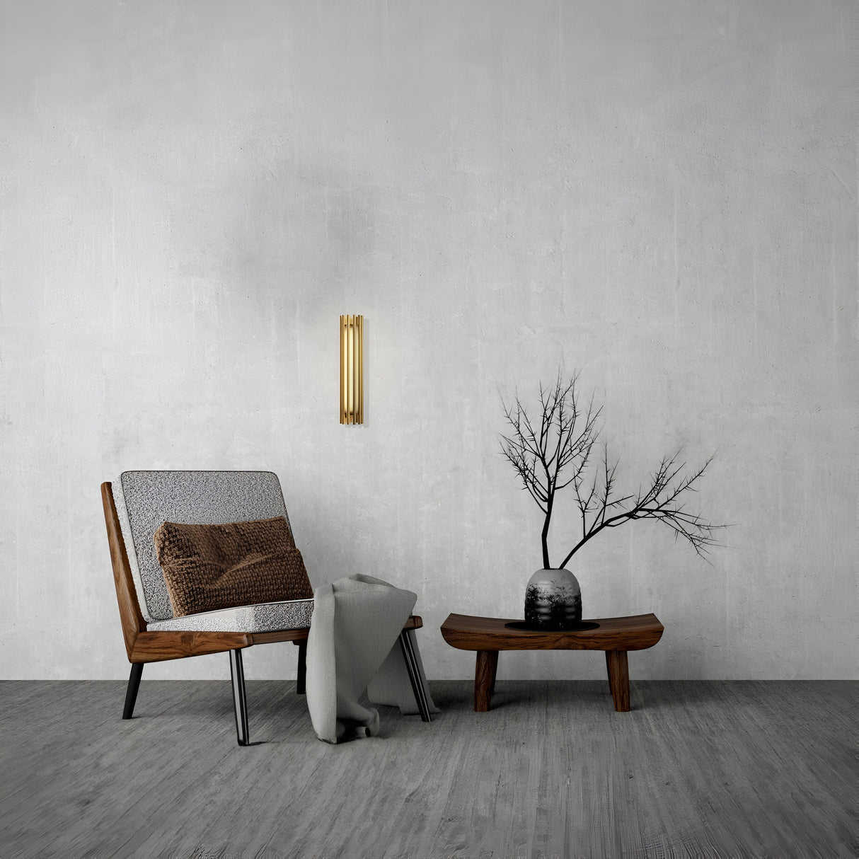 A minimalist living room features a wooden chair with a brown cushion, gray throw blanket, and wooden coffee table adorned with a vase of bare branches. The wall boasts the energy-efficient Sonata LED Wall Light 12W 3000K in brass against a gray textured surface.