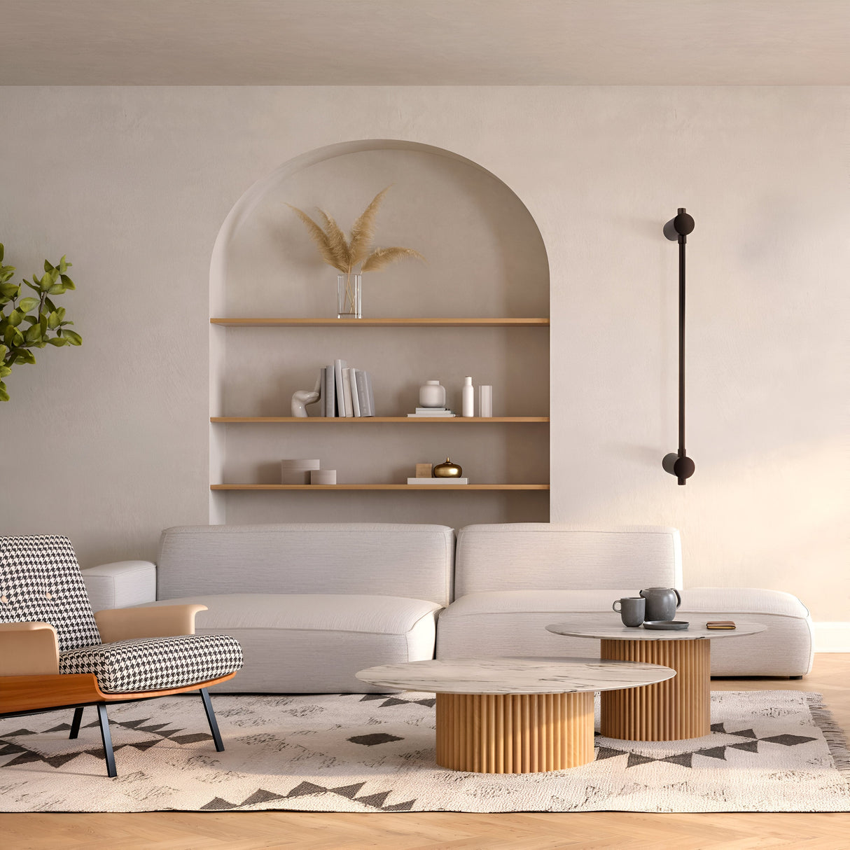 A modern living room has a white sectional sofa, two round wooden coffee tables, a black-and-white patterned armchair, and a built-in arched shelf for books and a vase. Subtle Rotta LED Wall Lighting highlights the space, complemented by a stylish geometric rug on the floor.