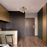 The modern kitchen and entryway boast sleek dark gray and gold cabinetry, highlighted by the Dallas 12 Light Semi-Flush - Gold With Amber Glass chandelier. Wooden flooring supports two bar stools at the counter, and a gray entry door with intercom is accented by gold metal fittings.