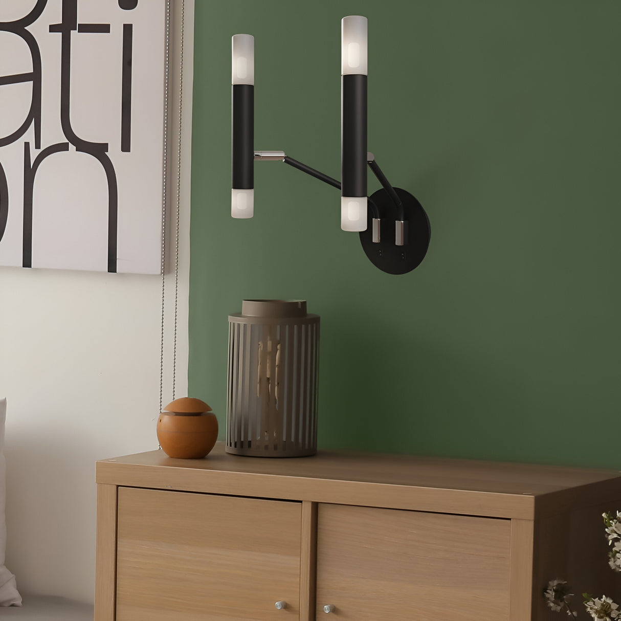 A modern design emerges with the Vigo 4 Light Wall Light in black, featuring two cylindrical lights on a green wall, above a wooden cabinet holding a vase and small container. Partial artwork adds intrigue to this industrial-inspired interior.