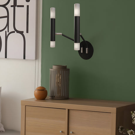 A modern design emerges with the Vigo 4 Light Wall Light in black, featuring two cylindrical lights on a green wall, above a wooden cabinet holding a vase and small container. Partial artwork adds intrigue to this industrial-inspired interior.