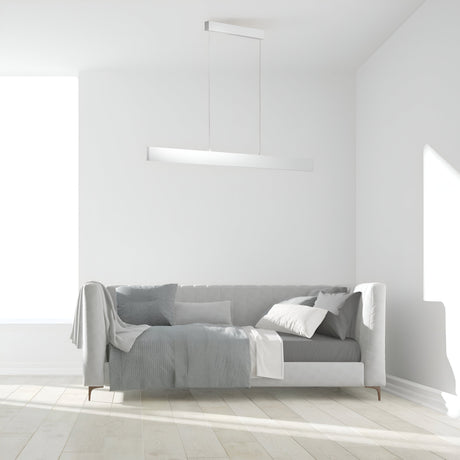 A minimalist living room includes a light gray sofa with cushions and a blanket. The Step LED Long Linear Suspension Light 4000K 30W - White adds modern flair, while natural light from a large window illuminates the light wooden floor, keeping the room bright.