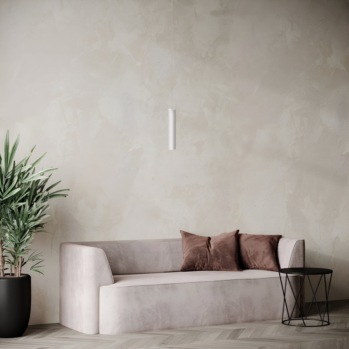 A minimalist living room showcases a light gray sofa adorned with two brown pillows, paired with a round black side table and a green potted plant. The Focus Single Pendant Light in white elegantly hangs from the ceiling against a textured, neutral-toned wall, exemplifying modern decor.