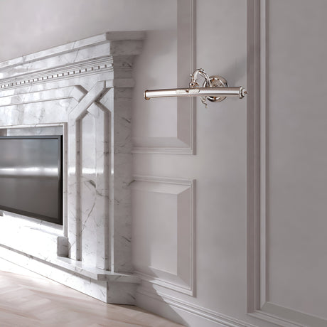 The elegant room showcases a polished marble fireplace with geometric designs, accented by a Picasso Classic Picture Light in gold. A modern flat-screen TV is set inside the fireplace, and a sleek chrome wall-mounted light fixture adorns the neighboring wall. The floor is light-colored wood.