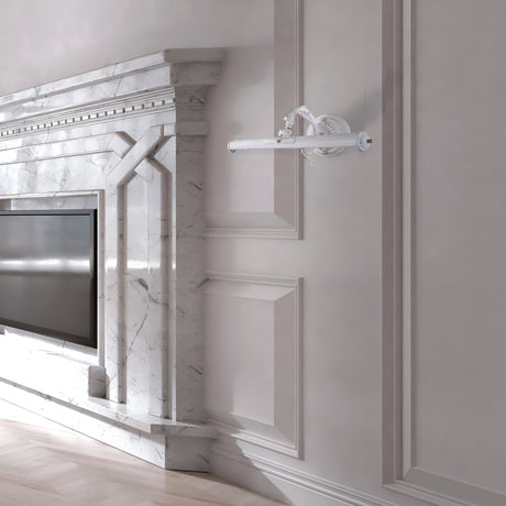 The room features an elegant marble fireplace with intricate detailing and a built-in flat-screen TV. A Picasso Classic Picture Light - White adds vintage charm, enhancing the luxurious design. A decorative wall sconce adorns the light gray paneled wall, and the polished wooden floor completes the look.
