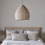 Jahari Woven Jute Pendant Light in natural dome shape with coarse open weave and rust cord, hanging above a bed with linen cushions in a neutral bedroom.