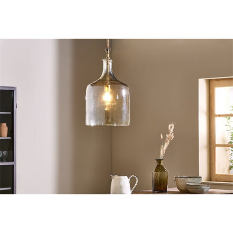 Kalsi Large Recycled Glass Pendant Light in Lustre finish, a tall jar-shaped shade with brass collar and visible lampholder, shown lit above a dining table in a warm-toned room.