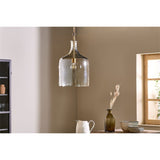 Kalsi Large Recycled Glass Pendant Light in Lustre finish, a tall flagon-shaped glass shade with brass collar and visible lampholder, hung in a dining area with a wooden table and decor nearby.