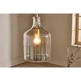 Kalsi Large Recycled Glass Pendant Light in Lustre finish, tall flagon-shaped glass shade with brass collar and exposed bulb, hung in a neutral-toned room corner near a window.