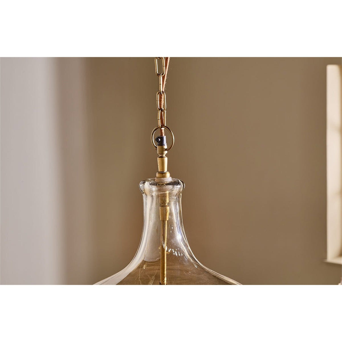 Kalsi Large Recycled Glass Pendant Light in Lustre, close-up of the flagon-shaped shade with smoky gold shoulder, brass collar, chain, and visible lampholder stem against a neutral wall.