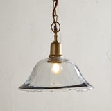 Keju Recycled Glass Pendant Light in Clear with a rippled, bubbled bell-shaped shade, brass collar and chain, and rust fabric flex, shown on a plain light background.