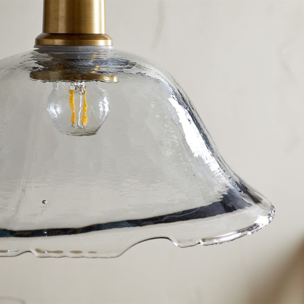 Close-up of the Keju Recycled Glass Pendant Light showing its clear, bubble-textured glass shade with rippled rim and brass collar and stem.