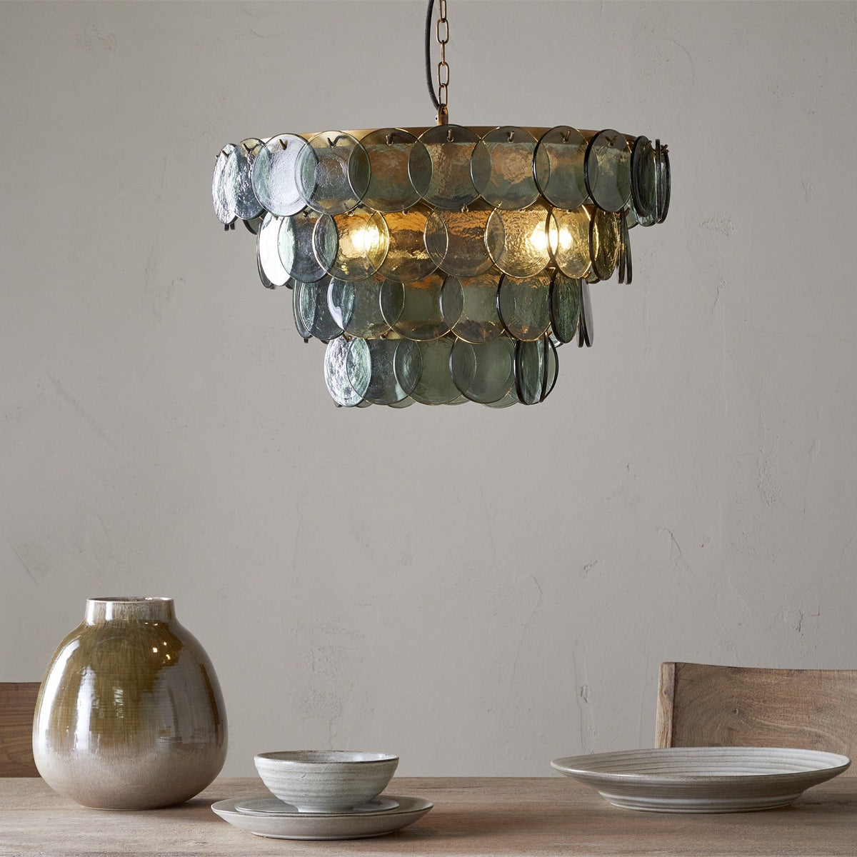 Kagitha Large 3 Light Recycled Glass Chandelier in Green, tiered round glass discs in brass frame hanging above a dining table in a light-toned room.