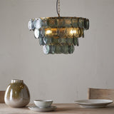 Kagitha Large 3 Light Recycled Glass Chandelier in Green, tiered round glass discs in brass frame hanging above a dining table in a light-toned room.