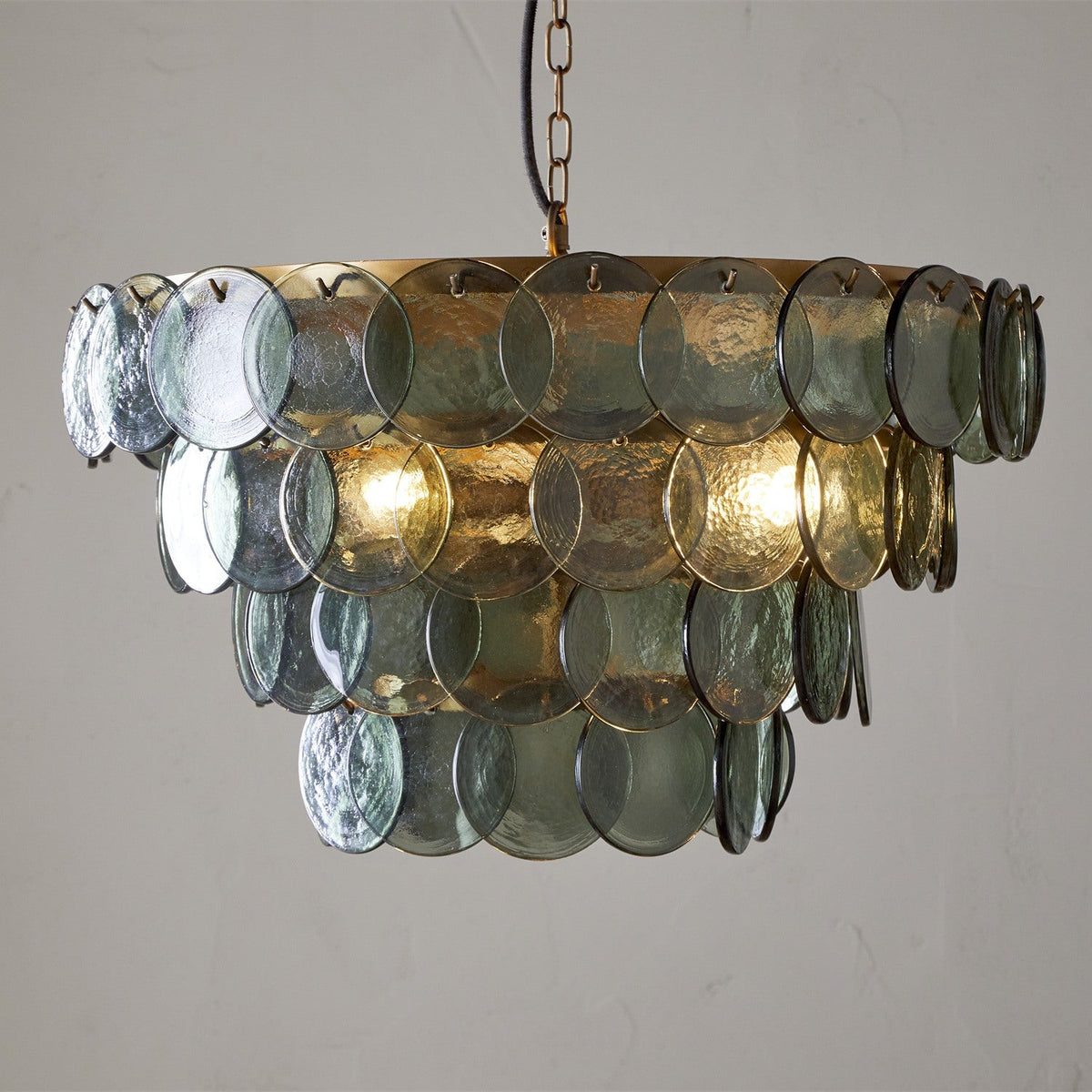 Kagitha Large 3 Light Recycled Glass Chandelier in Green, with four tiers of overlapping round green glass discs hooked onto a brass frame, hung on a chain against a plain background.