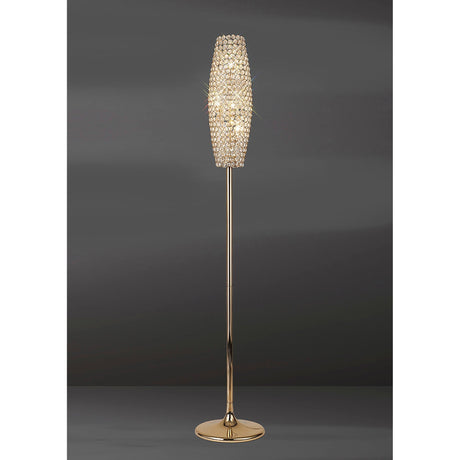 The Kos 4 Light Crystal Floor Lamp in French Gold features a slim stand and a tall, oval crystal-accented shade, glowing brilliantly against a dark gray backdrop.