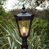 Victorian Manor black lantern head with 77mm fitting, glass panels, and lit bulb, mounted outdoors amid greenery.