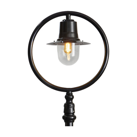 Cast Iron Railway Lantern head in black with clear glass globe and lit bulb, shown mounted within a circular hoop on a post for scale, plain white background.