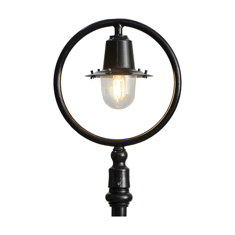 Cast iron railway lantern head in black with clear glass shade and visible bulb, shown mounted within a black hoop and post for scale on a plain white background.