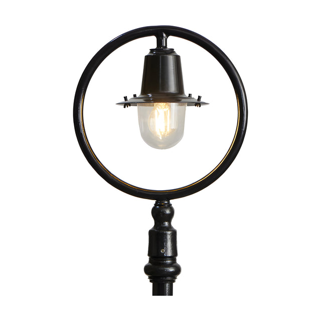 Cast iron railway lantern head in black with clear glass shade and visible bulb, shown mounted within a black hoop and post for scale on a plain white background.