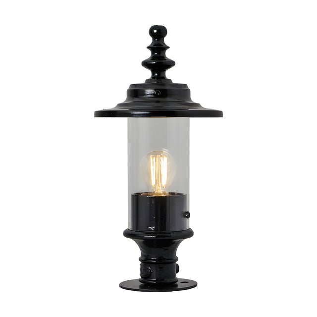 Cast iron Georgian lantern head in black with clear glass cylinder, ornate finial top and 44mm spigot fitting, shown lit on a black pedestal base against a plain white background.