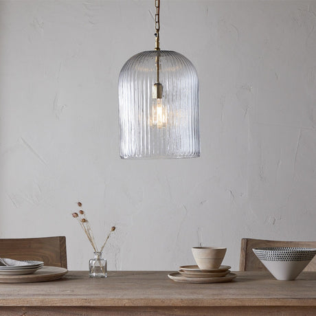 Lumina Large Fluted Glass Pendant Light in clear ribbed glass with brass fitting, hung above a wooden dining table set with ceramic bowls and plates.