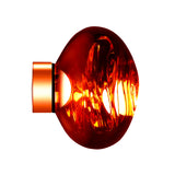The Lava Small LED Wall & Ceiling Light - Copper is a round, translucent amber glass fixture with a copper-finished shade on the left, set against a white background. It reflects light, creating glowing highlights and molten volcanic swirls inside.