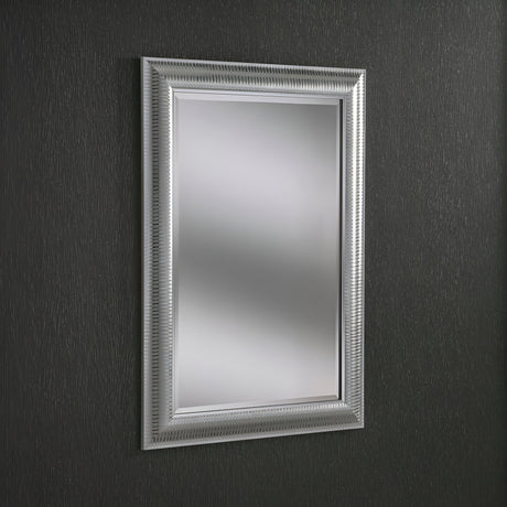 The Veris Rectangle Wall Mirror - Silver, featuring a textured silver frame, hangs on a dark, textured wall. Its intricate design adds elegance to the minimalist setting, while the dark tone of the wall mirror perfectly contrasts with its reflective surface.