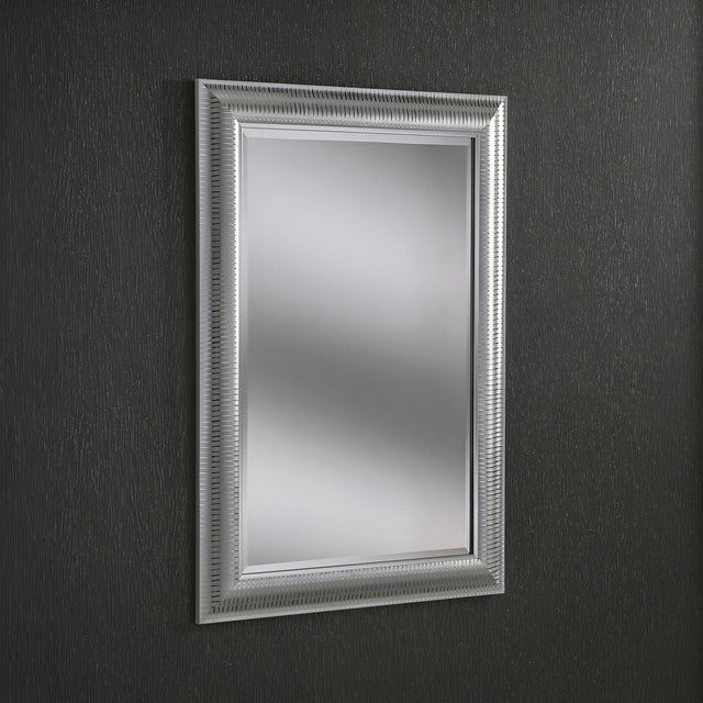 The Veris Rectangle Wall Mirror - Silver, featuring a textured silver frame, hangs on a dark, textured wall. Its intricate design adds elegance to the minimalist setting, while the dark tone of the wall mirror perfectly contrasts with its reflective surface.
