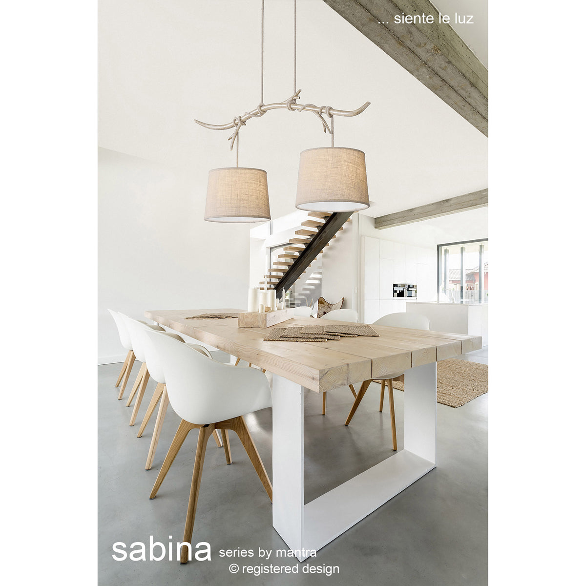 Sabina 2 Light E27 Pendant Light with beige linen drum shades hung from a branch-like imitation wood bar, shown above a wooden dining table in a bright interior.