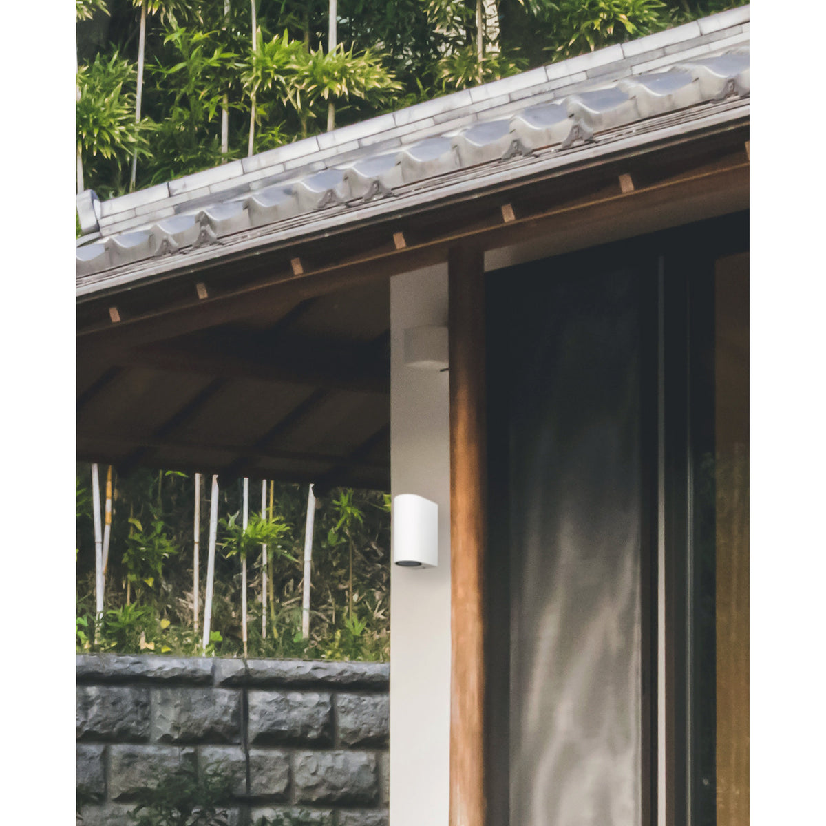 Kandanchu 2 Light round outdoor wall light in sand white aluminium, mounted on a timber post beside a dark doorway under a tiled eave.