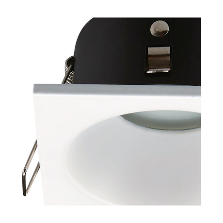 Close-up of the Comfort IP54 square downlight in matt white aluminium, showing the shallow square face, GU10 lamp holder, and spring clips against a black inner housing.