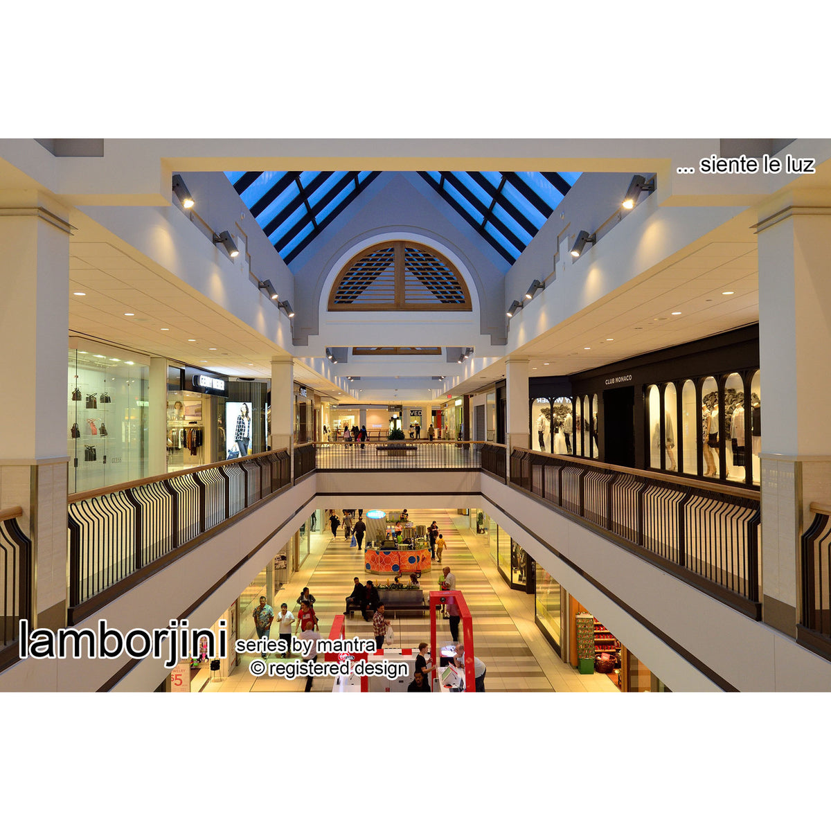 Recessed round spotlights, 93mm white polycarbonate finish, fitted throughout a shopping mall's white ceiling with angled beams lighting the walkways below.