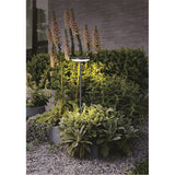 Akita IP54 Bollard Light, 60cm sand black aluminium post with round LED head, shown illuminating a planted garden bed beside a stone wall.