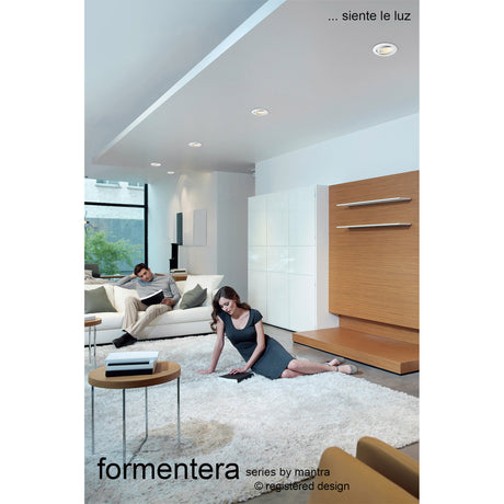 Formentera recessed downlights with matt white bezels installed in a living room ceiling, illuminating a neutral interior with sofa, rug and wood-panelled wall.