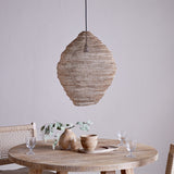 Mukuni Large Wire Lampshade in brass-toned knitted mesh, pendant style with a lantern silhouette, shown above a wooden dining table with tableware and a vase.