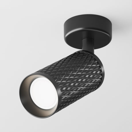 The Focus Design Single Spotlight - Black is a modern, black cylindrical track light with a textured diamond pattern, mounted on a white ceiling. It features a GU10 base for efficient illumination and emits a bright glow.
