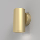 The FOCUS S Down Wall Light in matte gold boasts an industrial-inspired cylindrical design, mounted on a plain backdrop. It casts a rightward shadow while offering customizable lighting for any space.