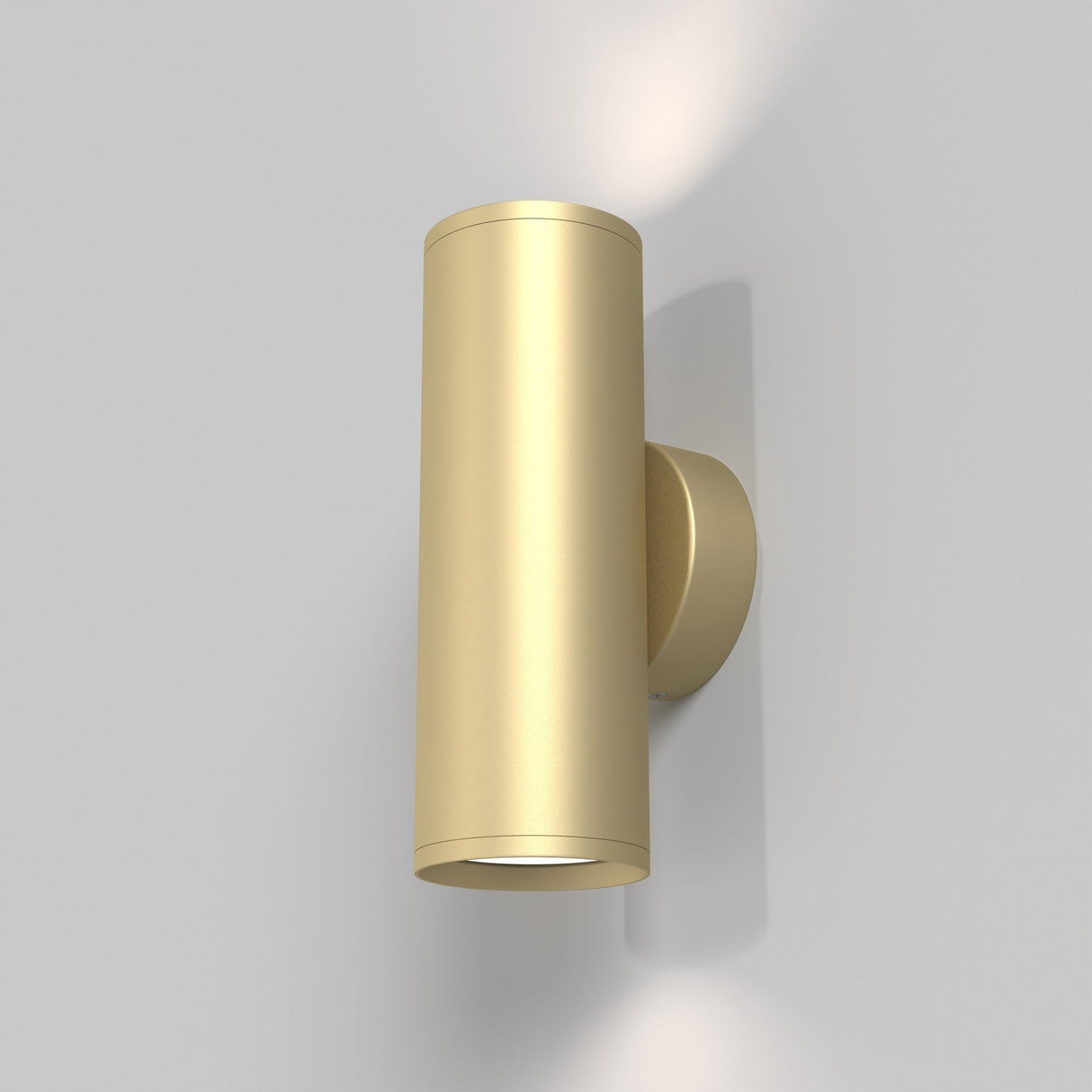 The FOCUS S Up & Down Wall Light in matte gold boasts a sleek cylindrical design with a small circular base, providing elegant lighting against a neutral gray backdrop.