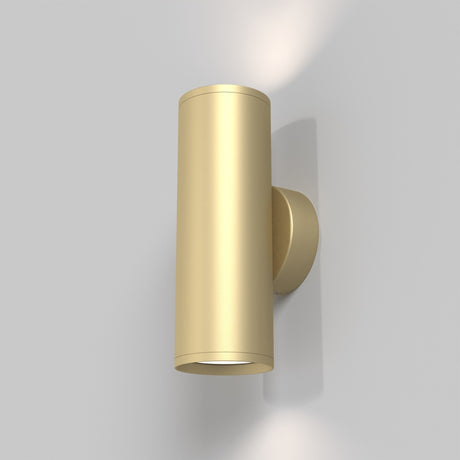 The FOCUS S Up & Down Wall Light in matte gold boasts a sleek cylindrical design with a small circular base, providing elegant lighting against a neutral gray backdrop.