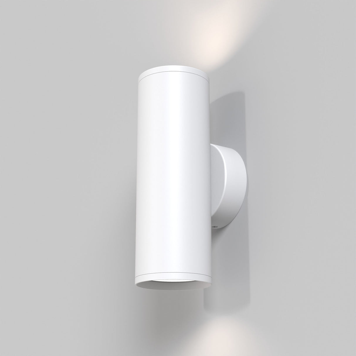 The FOCUS S Up & Down Wall Light in matte white, mounted on a light gray wall, uses GU10 bulbs to emit a soft glow, illuminating both the top and bottom.