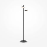 The Fad LED Floor Lamp in black features a minimalist design with a round base and tall slender pole, supporting two differently sized circular light fixtures. One fixture faces upwards while the other angles to the side, providing soft, energy-efficient lighting against a white backdrop.