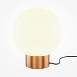 The Basic Form Table Lamp features a modern design with a gold metallic base and a round white frosted glass shade. It includes a black power cord and is set on a plain white background, emphasizing its sleek style.