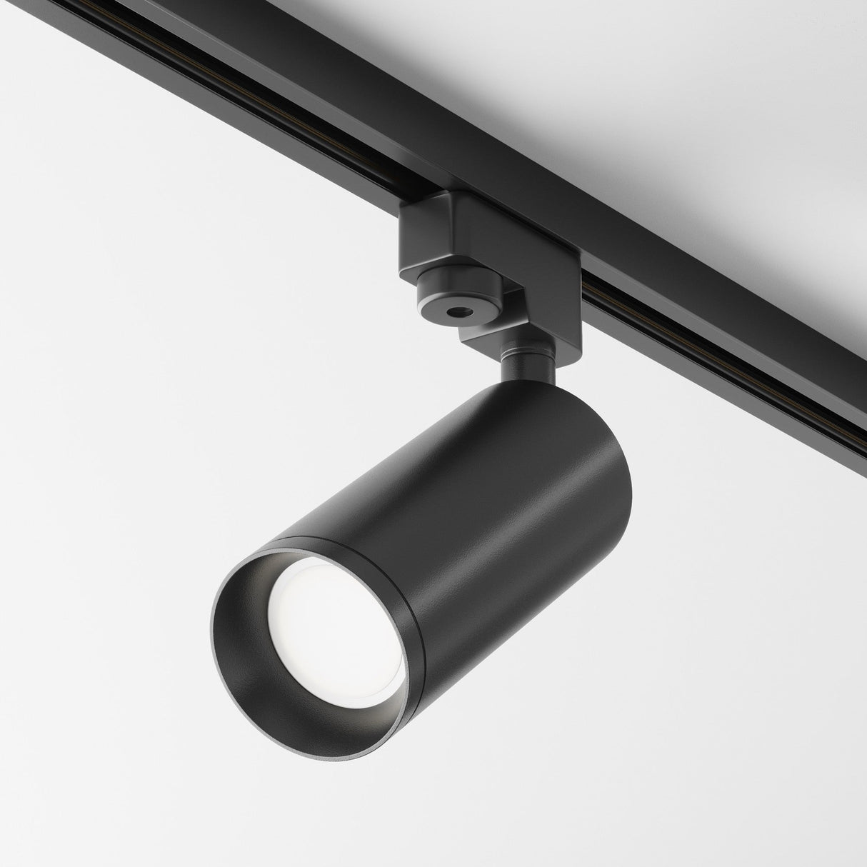 The Focus Single Phase Unity Track Spotlight - Black, with its sleek cylindrical pivoting head, mounts on ceilings for adjustable lighting direction. It uses GU10 light bulbs to ensure visual comfort against a plain white ceiling backdrop.