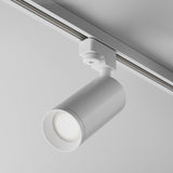 The Focus Single Phase Unity Track Spotlight in white is mounted on a ceiling rail, directing light downward. Its modern cylindrical design and swivel mechanism enhance its minimalist aesthetic, offering flexible illumination options.