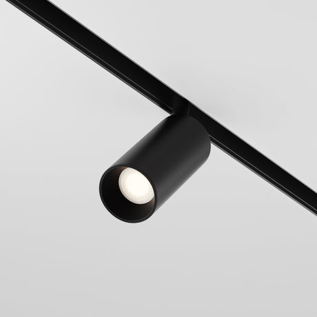 The Focus LED Magnetic Exility Track Spotlight 5W 3000K - Black, with its cylindrical design, mounts on a ceiling track to cast low glare light downward over a light gray backdrop, showcasing its sleek and modern minimalism.