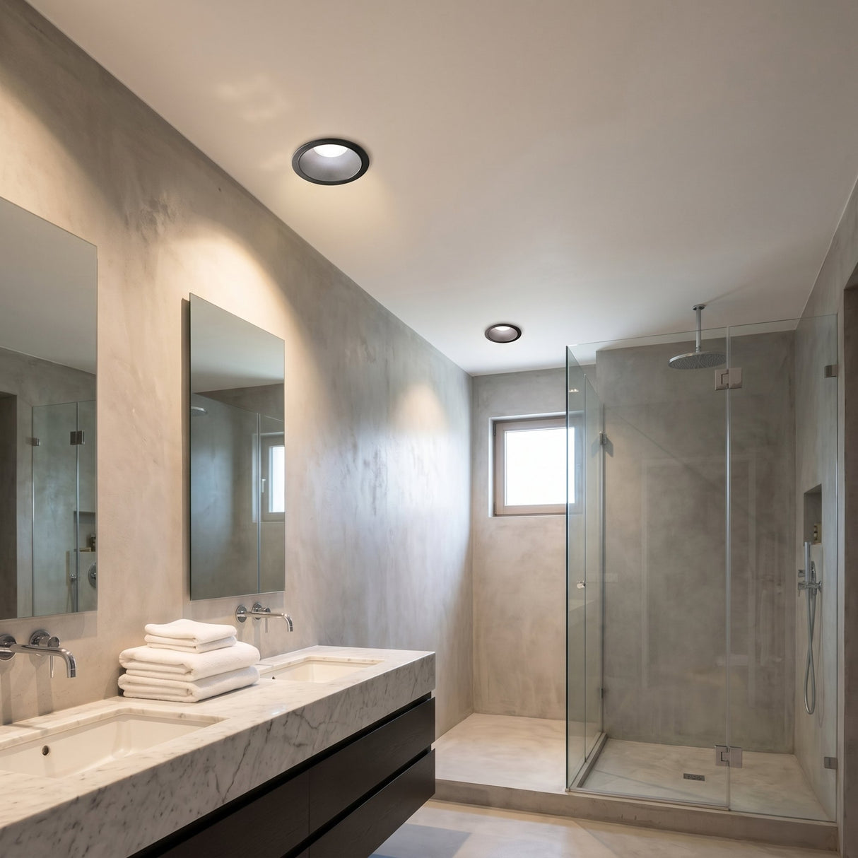 Ideal Lux Sally LED recessed downlight in matt black with IP65 rating, installed in a marble bathroom ceiling above the vanity and walk-in shower.