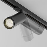The black Focus Zoom LED Single Phase Unity Track Spotlight 12W 3000K is mounted on the ceiling, casting downwards light with a sleek, cylindrical design and adjustable zoom feature, attached to a single-phase track system for flexible positioning.