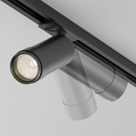 The Focus Zoom LED Dimmable Single Phase Unity Track Spotlight 12W 3000K in black is mounted on the ceiling, featuring a modern design with an adjustable scattering angle. Its minimalist look is highlighted against a light gray background with a single dimmable spotlight turned on.