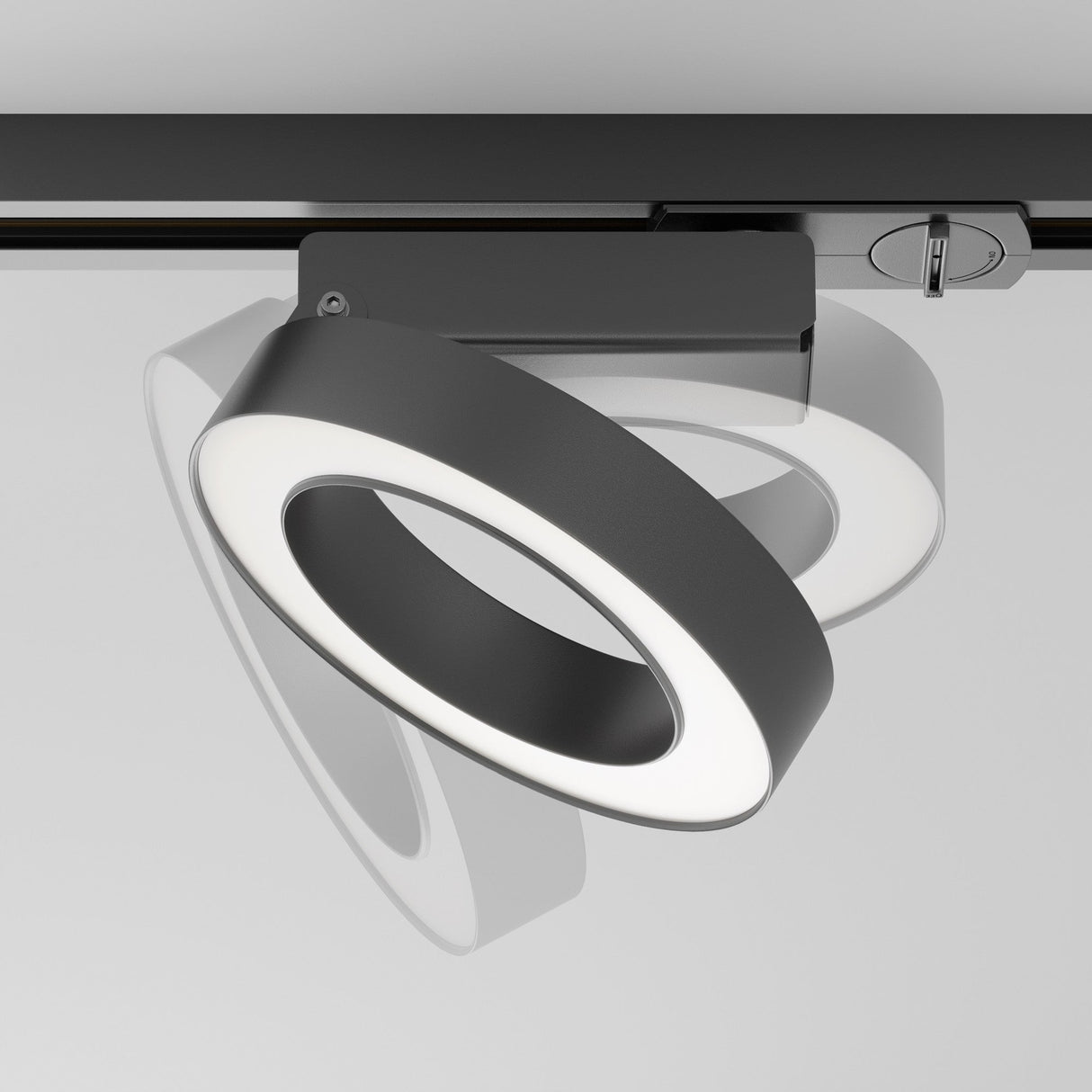 The Rim LED Single Phase Unity Track Spotlight 12W 4000K in black is a modern, circular ceiling light with a sleek frame. It emits neutral light and features an adjustable mount design, allowing it to be angled in various directions while casting shadows on the surface.